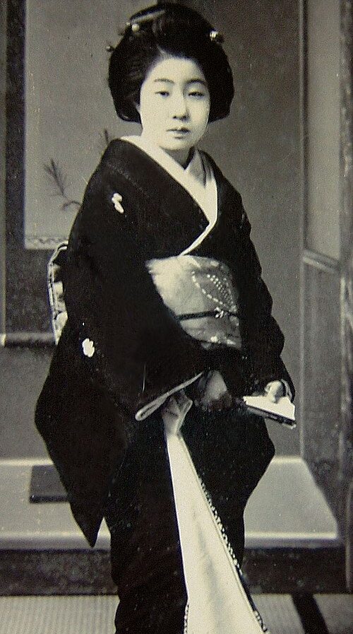 Ein junge Frau in einem traditionellen Kimono, vor einem neutralen Hintergrund.