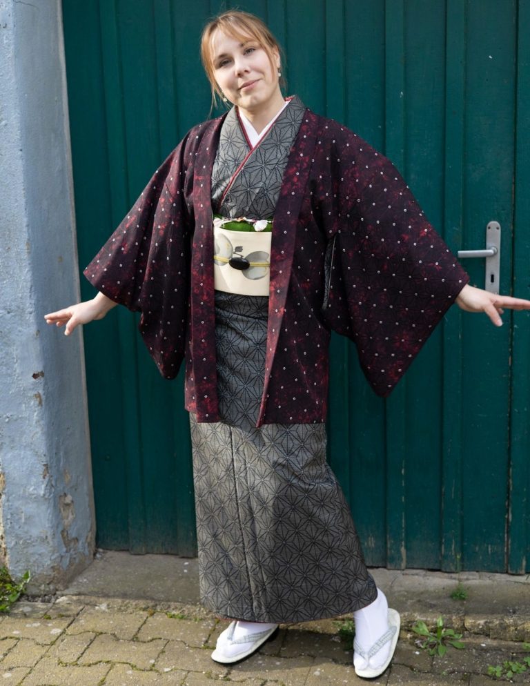 Frau im Kimono die ein Obidome trägt Frau in traditioneller japanischer Kleidung steht vor einer grünen Tür.